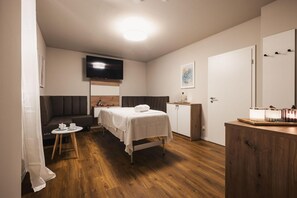 Une chambre d’hôtel avec un lit, une petite table sur laquelle se trouvent une tasse et une soucoupe, un canapé, un téléviseur fixé au mur et une armoire en bois avec un miroir.