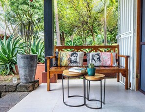 A wooden bench with cushions, a potted plant, and a book on a small table in a garden setting. - Serene Tamarindo Retreat with Shared Pool and Garden Views (Tamarindo)