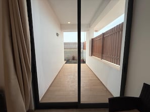 A narrow corridor with wooden flooring, a sliding glass door, and a view of a fenced backyard with potted plants.