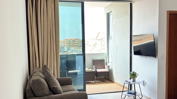 A modern living room with a sofa, a small table with a plant, and a TV mounted on the wall.