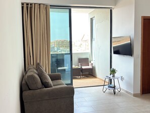 A modern living room with a sofa, a small table with a plant, and a TV mounted on the wall.