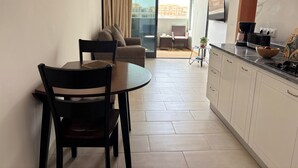 A modern kitchen with white cabinets, a dining table with chairs, and a small island with a bowl of fruit.