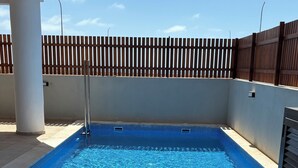 A swimming pool with a wooden deck, lounge chairs, and a table with drinks and a hat.