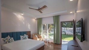 A bedroom with a large bed, a ceiling fan, a TV, and a view of the outdoors. - Corbett Hidden Paradise (Ramnagar)