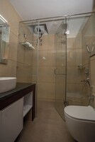 Moderni kylpyhuone, jossa on lasiseinällä varustettu suihku, valkoinen pesuallas ja wc.