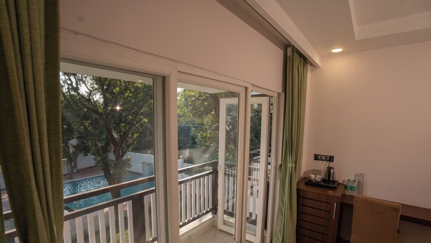 A room with a view of a swimming pool, a wooden desk with a chair, and a small cabinet. - Corbett Hidden Paradise (Ramnagar)
