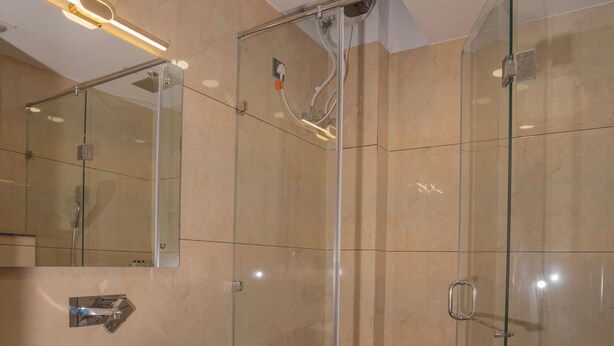 Un baño moderno con ducha de vidrio, lavamanos blanco y un espejo grande.