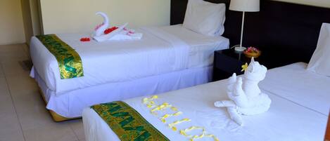 Two hotel beds with white linens, one with a green and gold headboard, and a towel sculpture on the right bed.
