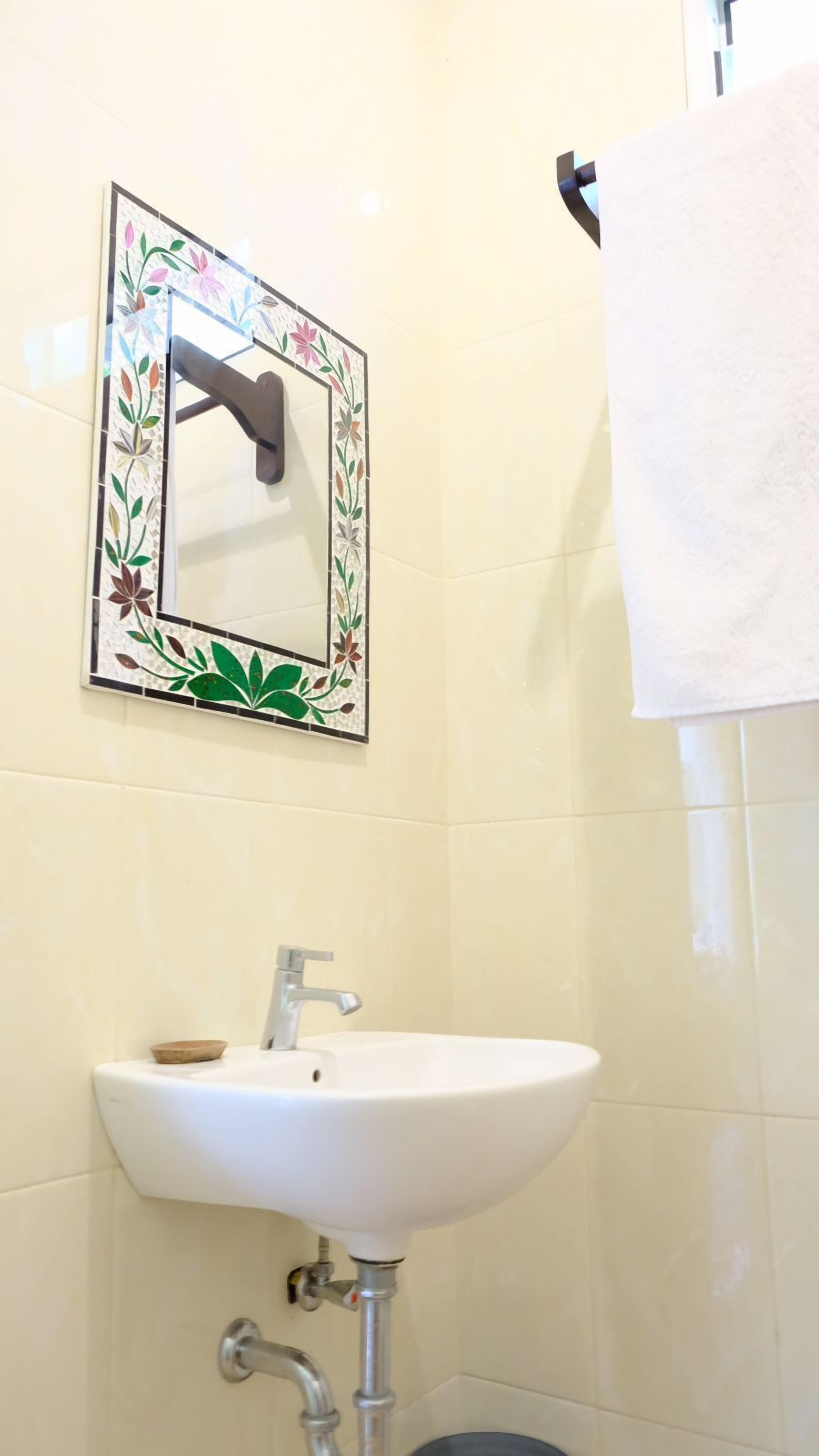 A bathroom with a white sink, a mirror with a floral frame, and a towel hanging on a rack.