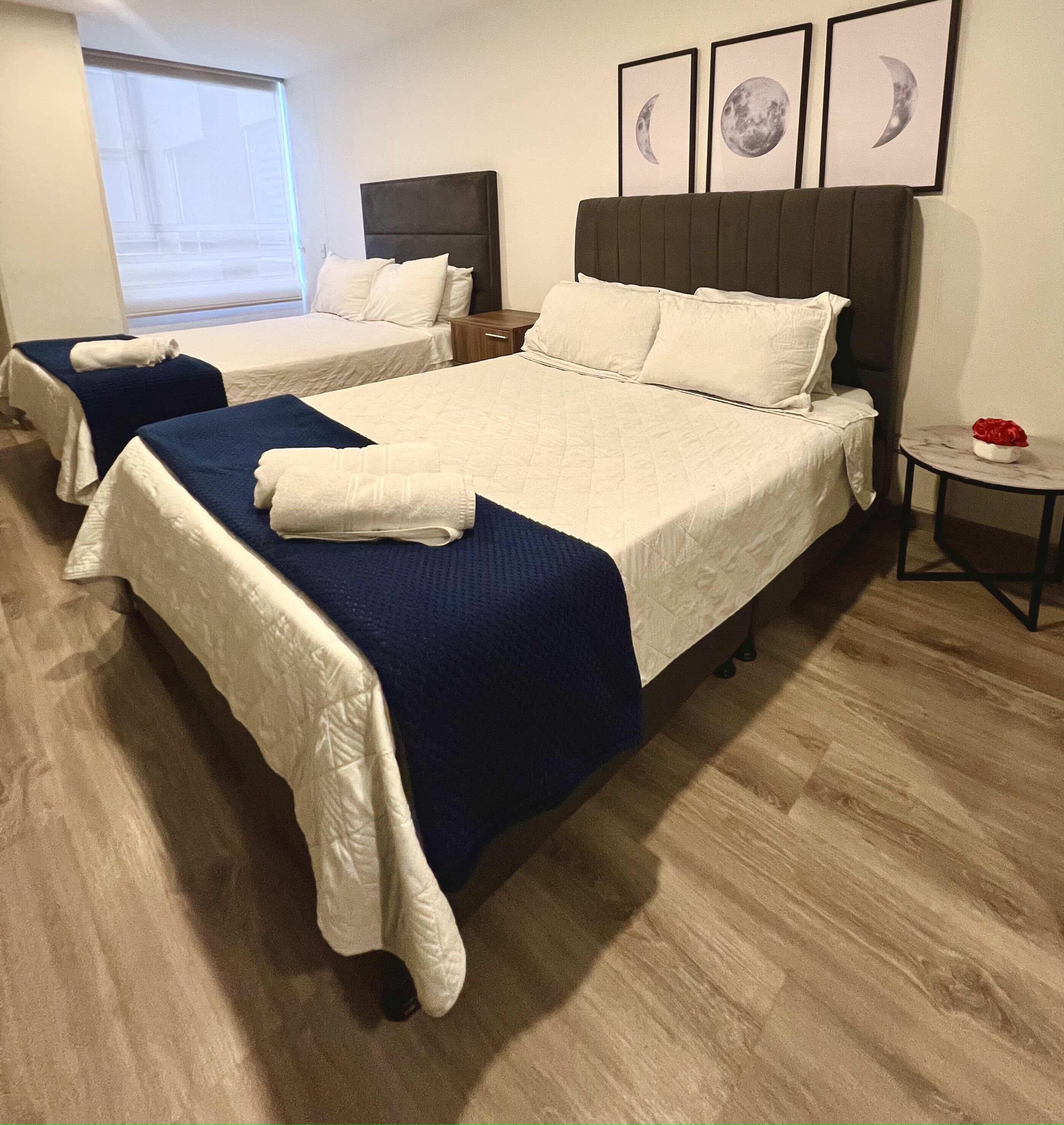 Hotelkamer met twee bedden, elk met witte lakens en blauwe dekens, een houten vloer en een tafeltje met een rood object.