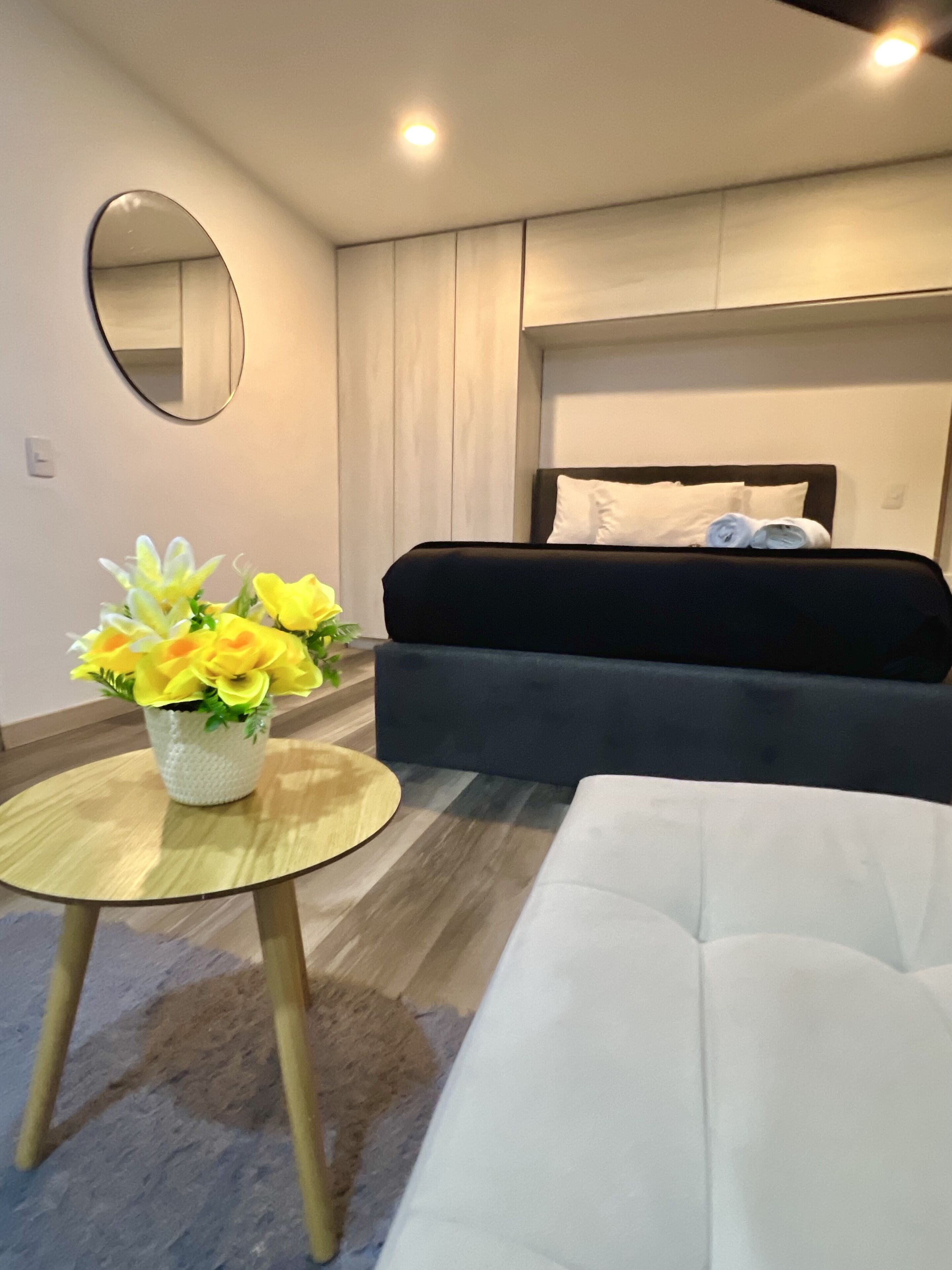 Un dormitorio moderno con una cama, una mesa redonda con un florero y un sofá blanco.