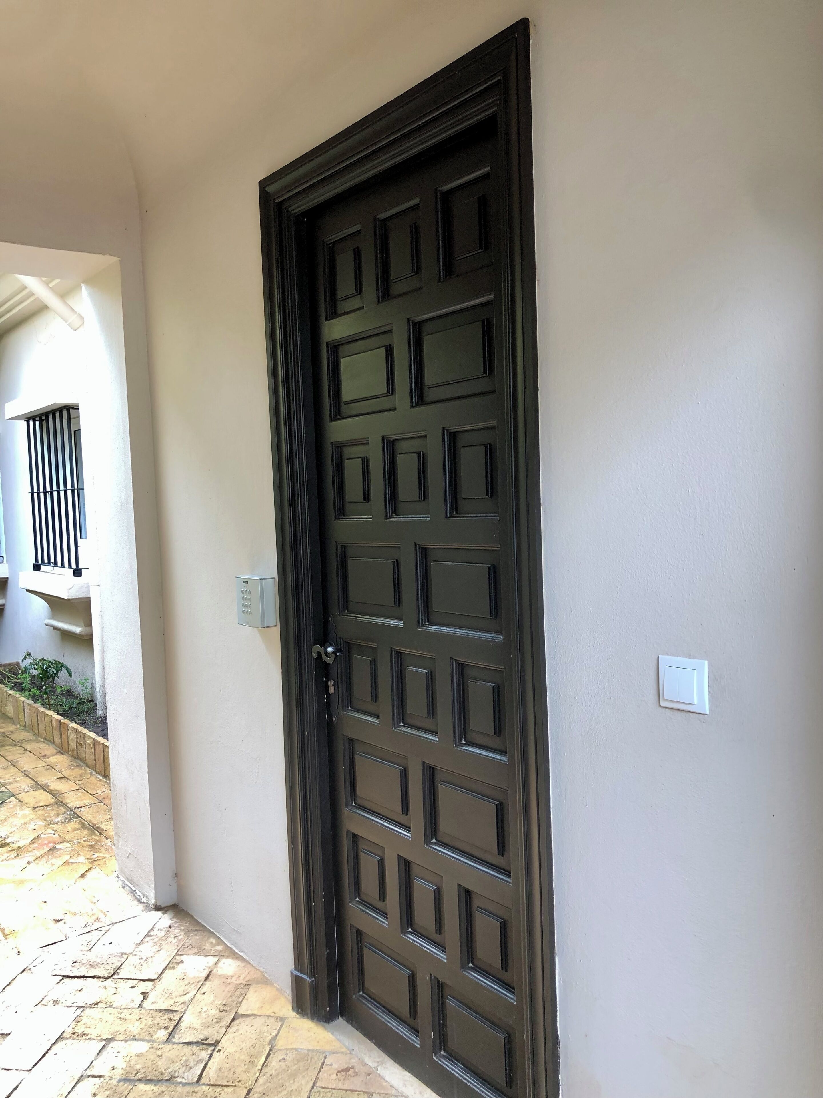 Une porte marron foncé ornée d’un motif quadrillé, un interrupteur et une boîte de sécurité fixés au mur.