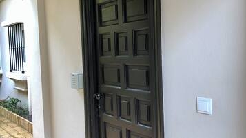 Une porte marron foncé ornée d’un motif quadrillé, un interrupteur et une boîte de sécurité fixés au mur.