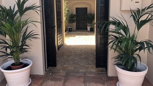 A pathway leading to a building with black doors and potted plants on either side. - PATIO ROOM SOTOGRANDE (sotogrande)