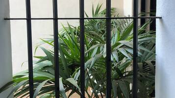 A window with metal bars, a white wall, and green plants outside.
