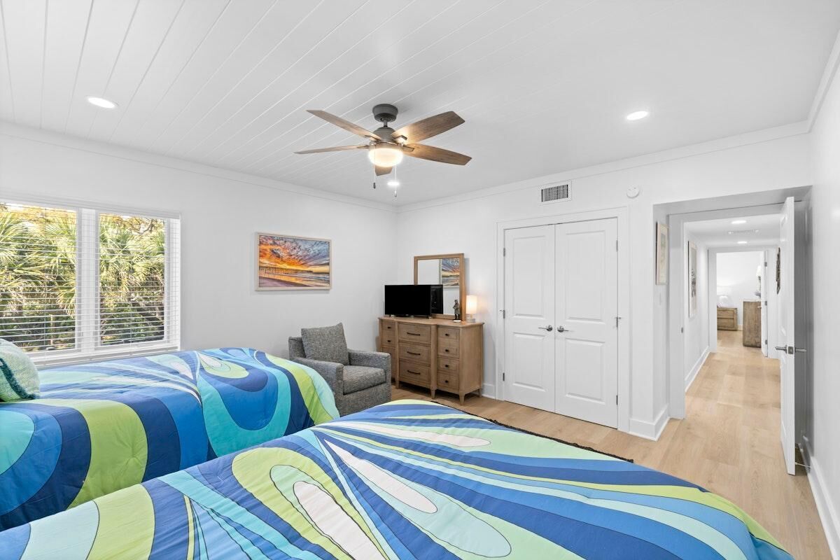 A bedroom with two beds, a ceiling fan, a television on a wooden cabinet, and a door leading to another room.