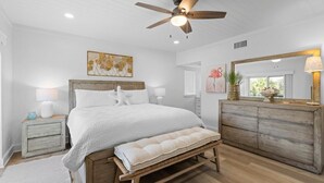 Ein Schlafzimmer mit Bett, Nachttischen, einer Bank, einem Deckenventilator, einem Schminktisch und Bildern an den Wänden.