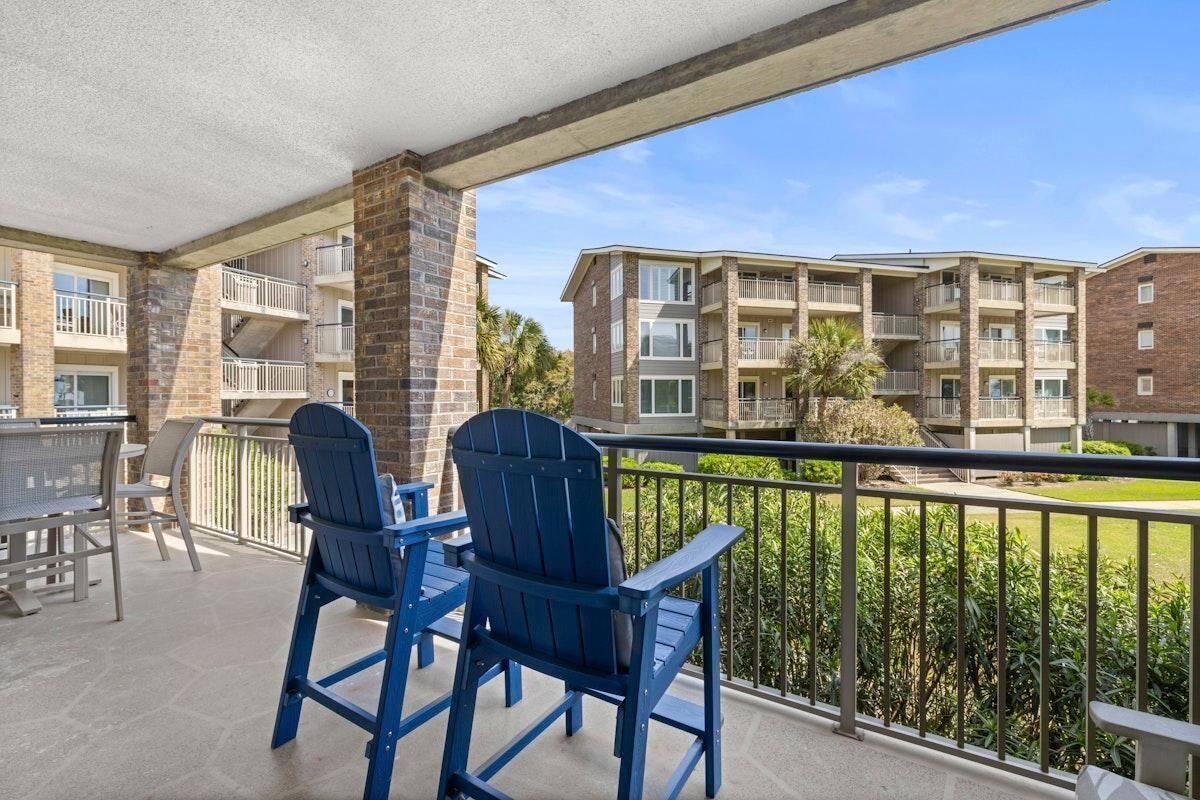 Ein Balkon mit zwei blauen Adirondack-Stühlen, einem Tisch und Blick auf mehrstöckige Gebäude mit Balkonen.