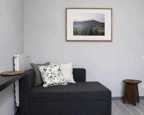 Uma sala de estar moderna com um sofá cinzento, um quadro de uma paisagem, um radiador e um banquinho de madeira.
