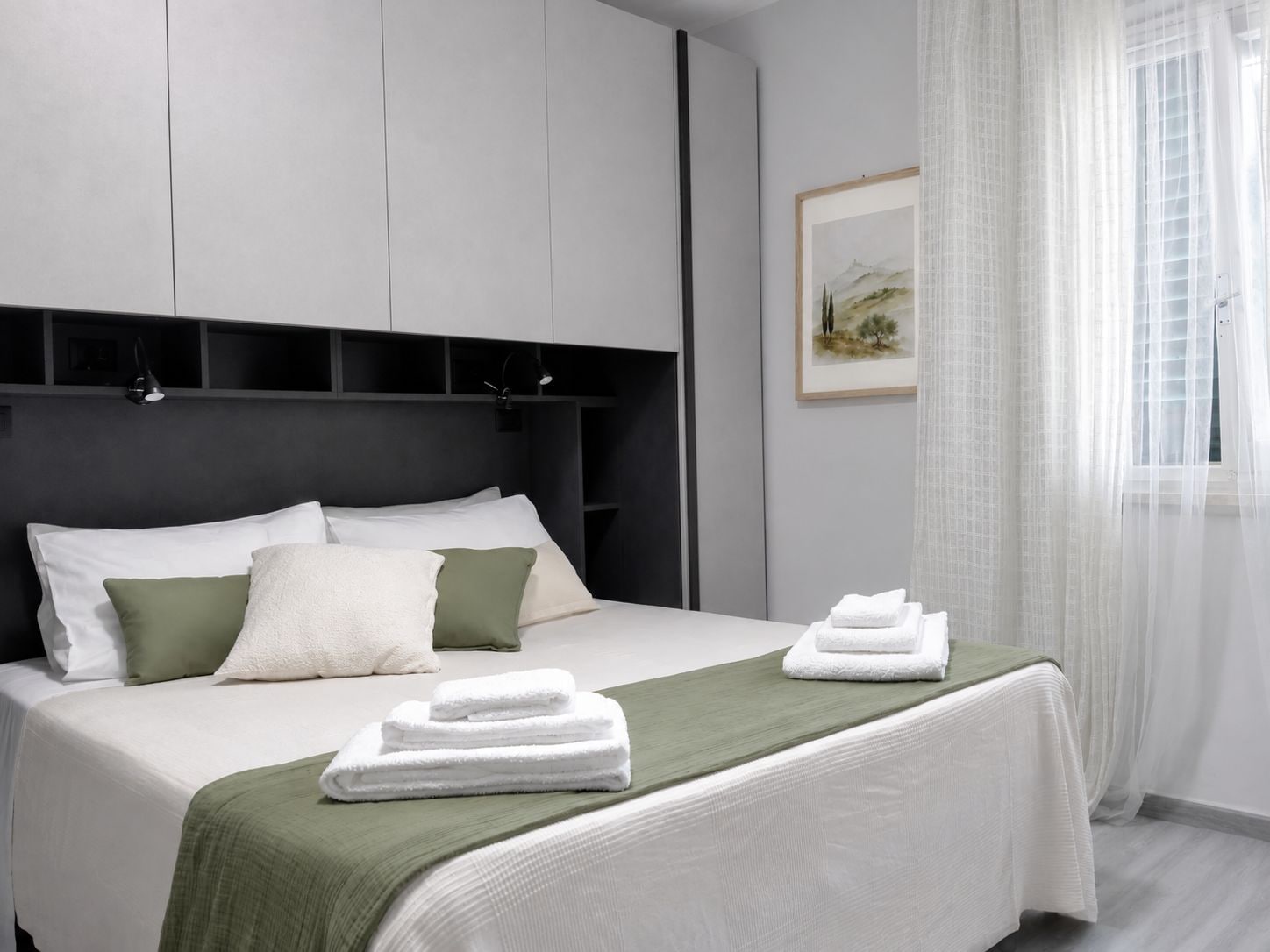 A modern bedroom with a bed, pillows, a green throw blanket, and neatly folded towels.