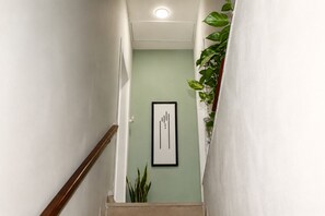 Een gang met een houten leuning, een lijstwerk abstract kunstwerk aan de muur en een potplant.