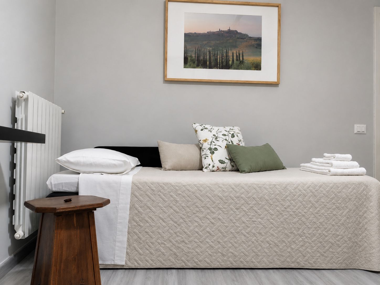 Une chambre à coucher avec un lit, des oreillers, une table de chevet, un radiateur et un tableau encadré accroché au mur.