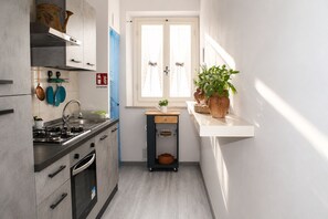 A narrow kitchen with a gas stove, oven, and a window with curtains. - WOW San Miniato! 2 Bedrooms Central Apartment (San Miniato)