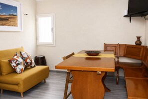 Uma área de jantar com mesa de madeira, cadeiras e um banco. Há um sofá com almofadas e um porta-retrato na parede.