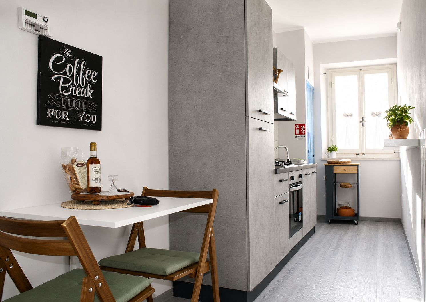 A modern kitchen with a white countertop, a coffee-themed wall art, and a dining area with a wooden table and chairs.