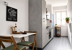 Cozinha moderna com bancada branca, uma obra de arte com tema de café na parede e área de jantar com mesa e cadeiras de madeira.