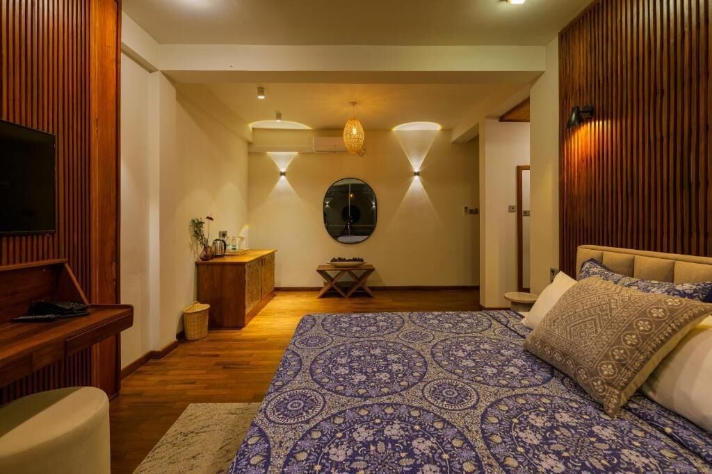 A bedroom with a large bed, a wooden headboard, a TV on the left, and a desk with a lamp.