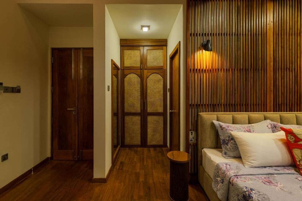 Ein Zimmer mit Holzboden, einem Bett mit floralem Bettbezug, einer Wandlampe und einer Holztür mit einem gewebten Paneel.