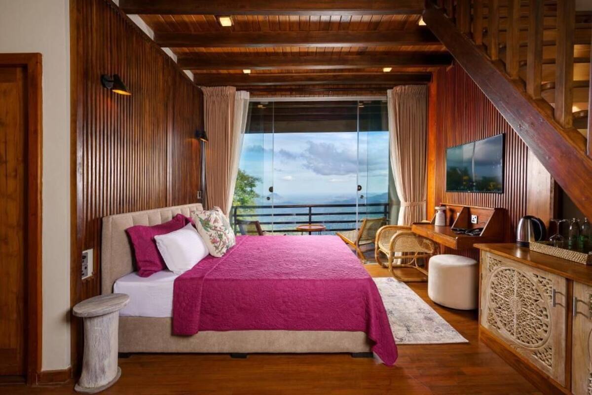 Un dormitorio con una cama grande, paredes de madera, un balcón con vistas y un televisor.