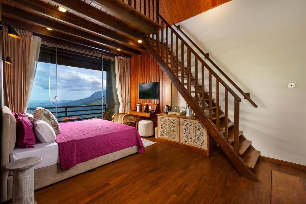 A bedroom with a large bed, wooden flooring, a staircase, and a TV.