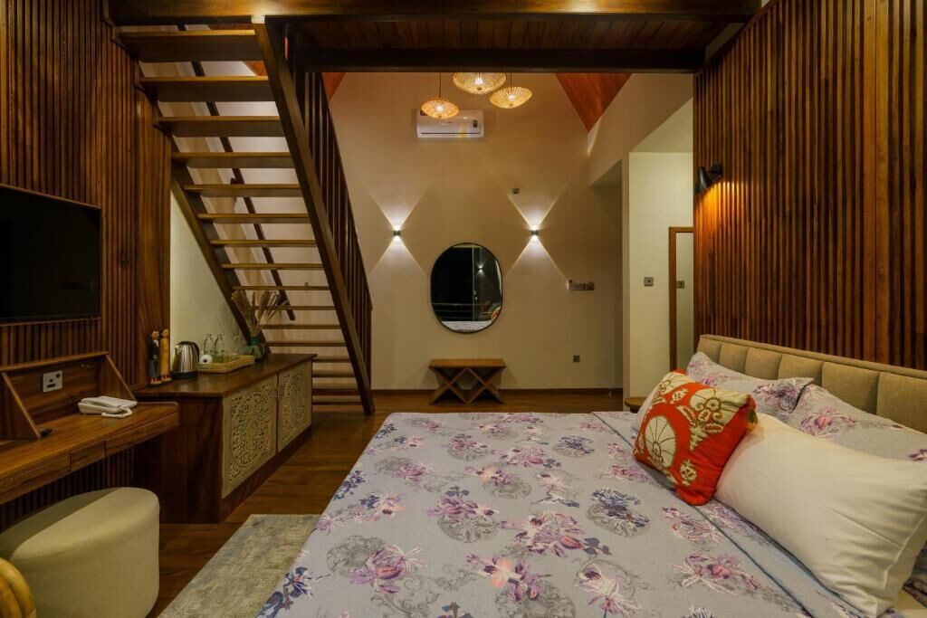 A bedroom with a wooden staircase, a bed with floral bedding, a bedside table, and a TV.