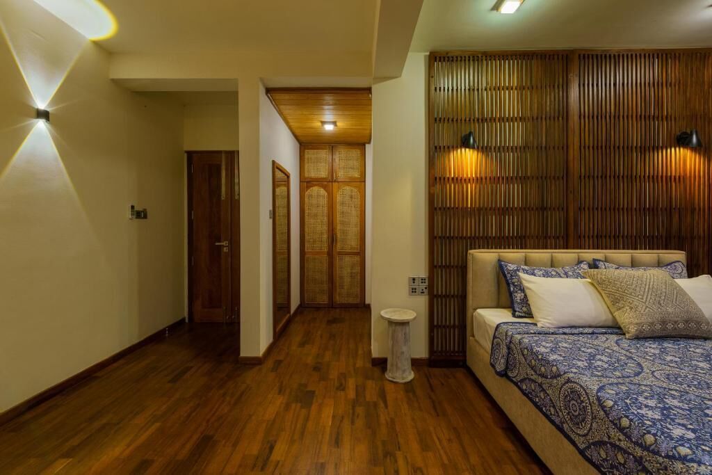 A bedroom with a wooden floor, a bed with patterned bedding, and a wall with vertical wooden slats.