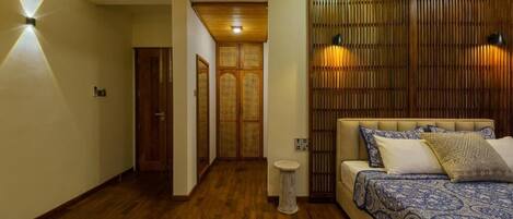 A bedroom with a wooden floor, a bed with patterned bedding, and a wall with vertical wooden slats.