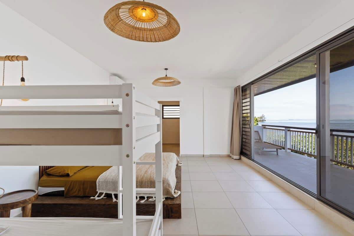 A modern bedroom with a bunk bed, a small desk, and a balcony with a view.
