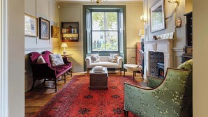 A traditional living room with a red patterned rug, a fireplace, and a large window with a view of greenery.