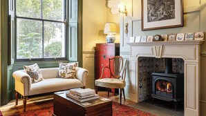 A cozy room with a fireplace, a sofa with patterned cushions, a wooden chair, and a red cabinet.