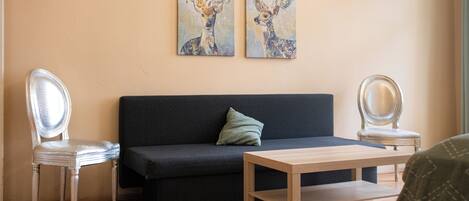 Une pièce comprenant un canapé de couleur sombre, deux fauteuils, une table en bois et deux tableaux représentant des cerfs, accrochés au mur.