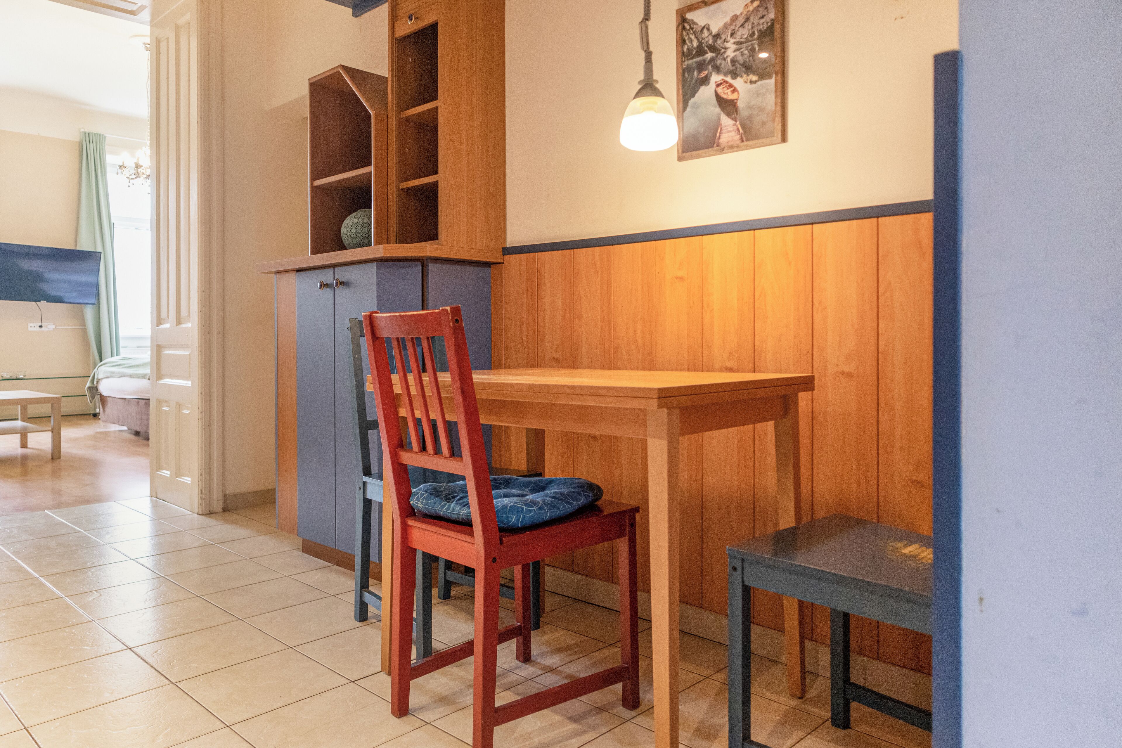A dining area with a wooden table, a red chair with a blue cushion, and a small table.
