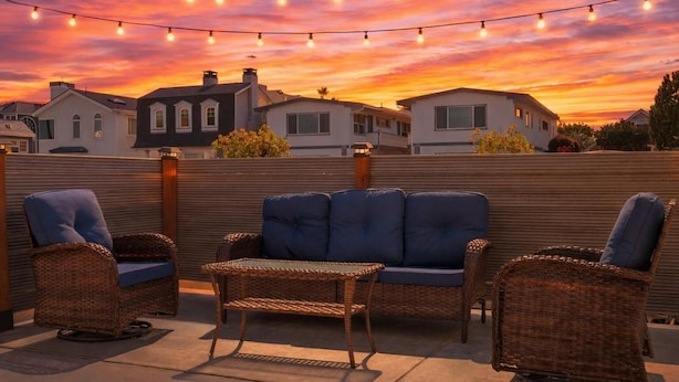 A rooftop patio with wicker furniture, string lights, and a sunset view. - 2BR Beach Getaway w/ Patio, AC, WiFi, W&D, Smart TV's & Steps to the Sand (Newport Beach)