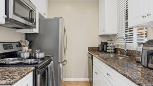 A modern kitchen with white cabinets, granite countertops, stainless steel appliances, and a built-in oven. - 2BR Beach Getaway w/ Patio, AC, WiFi, W&D, Smart TV's & Steps to the Sand (Newport Beach)
