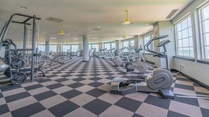 Et fitnesscenter med forskellig træningsudstyr, skakternet gulv og store vinduer.