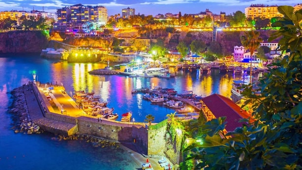 A coastal cityscape with a harbor, buildings, and a fortified wall. - Moon City (Antalya)