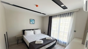 A modern hotel room with a large bed, a bedside table, a small desk, and a window with curtains. - Moon City (Antalya)