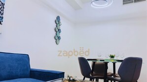 Un salon moderne avec un canapé bleu, une table basse en verre et un coin repas comprenant une table et des chaises.