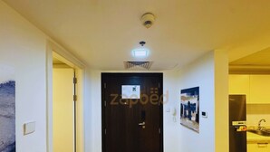 Un couloir avec un plancher en bois, une porte sombre et un coin cuisine équipé d’un réfrigérateur et d’un évier.