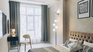 A modern hotel room with a large bed, a desk, and a chair. There is a window with curtains, a wall-mounted light fixture, and a framed artwork. - Lev bir (Baku)
